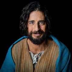 a man with long hair and beard wearing a blue shawl over his shoulders is smiling at the camera