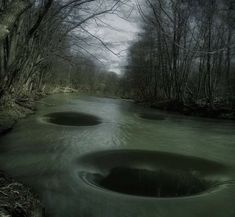 three round holes in the water surrounded by trees and grass, with dark clouds overhead