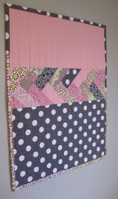 a pink and black wall hanging with polka dots on the bottom, along with a patchwork design