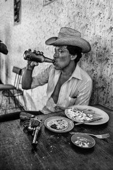 a man sitting at a table drinking out of a bottle while looking through a telescope