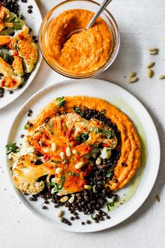 two white plates topped with food next to a bowl of hummus and black beans