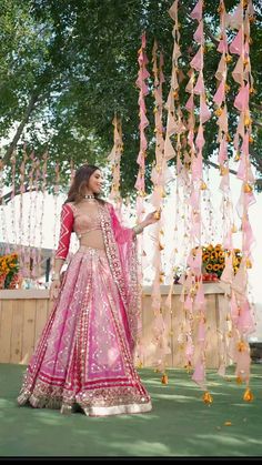 a woman in a pink lehenga standing under a tree with flowers hanging from it