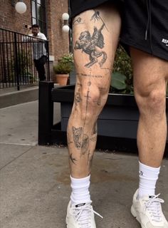 a man with tattoos on his legs and feet standing in front of a bench wearing white sneakers