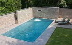 a pool with a water feature in the middle and lounge chairs around it, next to a stone wall