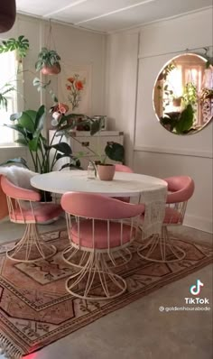 a dining table with pink chairs and potted plants in the corner next to it