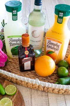 bottles of gin and orange juice on a wicker tray with limes, an avocado, and two lemons