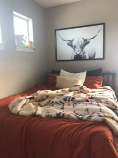 a bed with an orange blanket on top of it next to a framed cow head