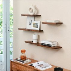 three wooden shelves on the wall above a desk with an open book and coffee cup