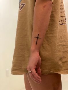 a person with a cross tattoo on their left arm and the other hand behind them