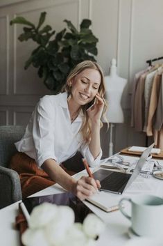 a woman sitting at a desk talking on the phone and working on her laptop computer