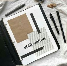 an open book sitting on top of a table next to some pens and pencils