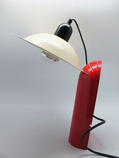 a red table lamp with a white shade on it and a black light plugged in