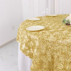 a gold table cloth with white plates and flowers on the table in front of it