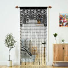 a living room with white walls and wooden flooring next to a large window covered in black lace