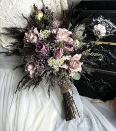 a bridal bouquet sitting on top of a white bed next to a black dresser