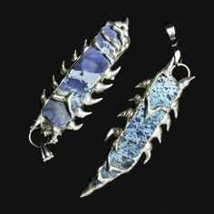 two pieces of jewelry sitting on top of a black surface with blue and white designs