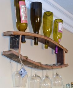 several wine bottles and glasses are hanging on the wall above a wooden shelf that holds three wine glasses