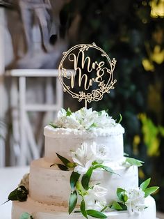 a wedding cake with white flowers and a mr and mrs topper on the side