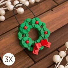 a lego christmas wreath ornament on a wooden table with white balls and string