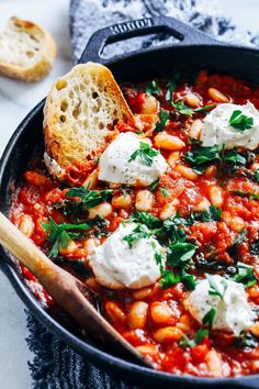 a skillet filled with beans and cheese on top of a white table next to bread