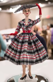 a doll wearing a dress and hat on display in a store or showroom with people walking around