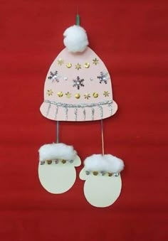 a paper hat and mittens are hanging on a red background with white pom - poms