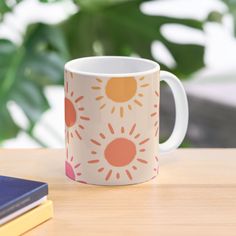 a coffee mug sitting on top of a wooden table next to a book and plant