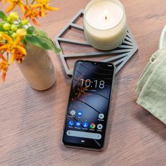 a cell phone sitting on top of a wooden table next to a vase with flowers