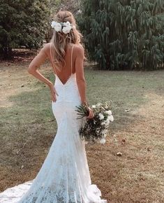 a woman in a wedding dress standing on the grass with her back to the camera