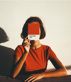 a woman sitting at a table holding up a red book with the word pantone on it