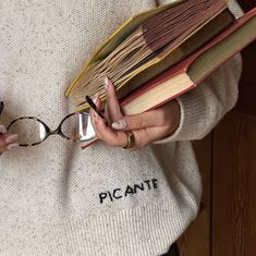 a woman holding a stack of books and reading glasses with her hands on top of them