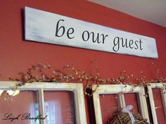 a sign that says be our guest hanging on the wall next to two window frames