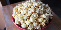 a red bowl filled with popcorn on top of a wooden table