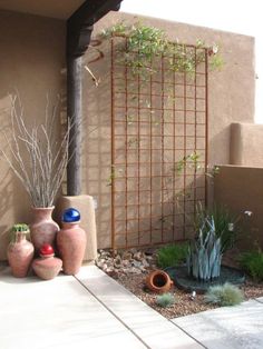 two vases are sitting on the ground in front of a wall with a trellis