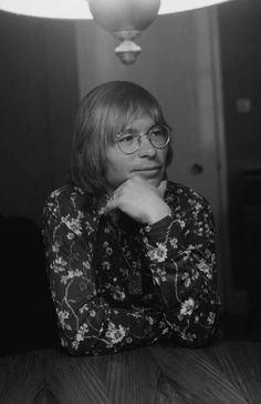 a black and white photo of a woman sitting at a table with her hand on her chin