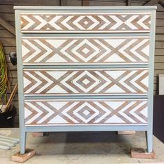 an old dresser is painted white and brown with geometric designs on the top, along with some wood planks