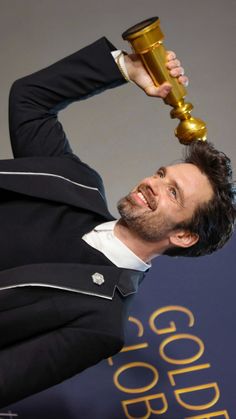 a man in a tuxedo holding an award up to his head with both hands