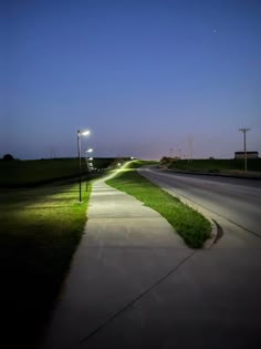 an empty street at night with lights on the side and grass in the foreground