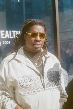 a man with dreadlocks and sunglasses standing in front of a storefront window