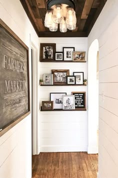 a hallway with white walls and wooden flooring, framed pictures on the wall and hanging lights