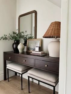 a wooden desk topped with a mirror and two vases next to a table lamp