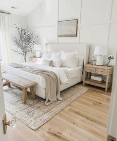 a large white bed sitting in a bedroom on top of a hard wood floor next to a window