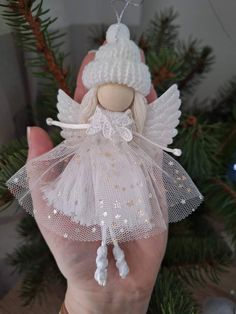 a hand holding a white angel ornament in front of a christmas tree branch