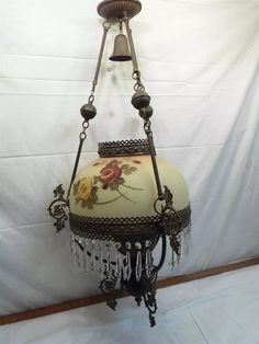 an old fashioned lamp hanging from a chain with flowers and chains attached to the light fixture