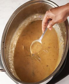 a person stirring something in a pot with a ladle on the side and another hand holding a spoon