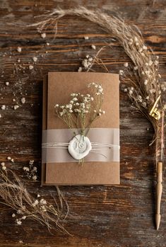 a small card with flowers on it next to a pen and some dried plants in the background