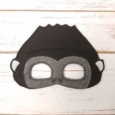 a black mask with two holes in the middle on a white wooden background and wood planks behind it