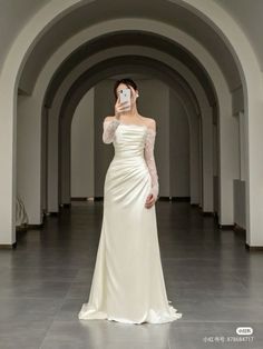 a woman in a white dress taking a selfie with her cell phone while wearing an off the shoulder wedding dress