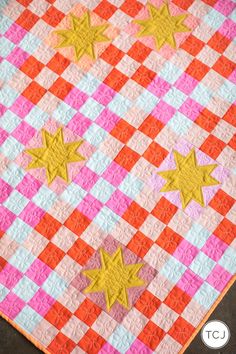 an orange, pink and yellow quilt with stars on the top is sitting on a table