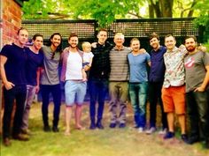 a group of men standing next to each other in front of a brick wall and tree